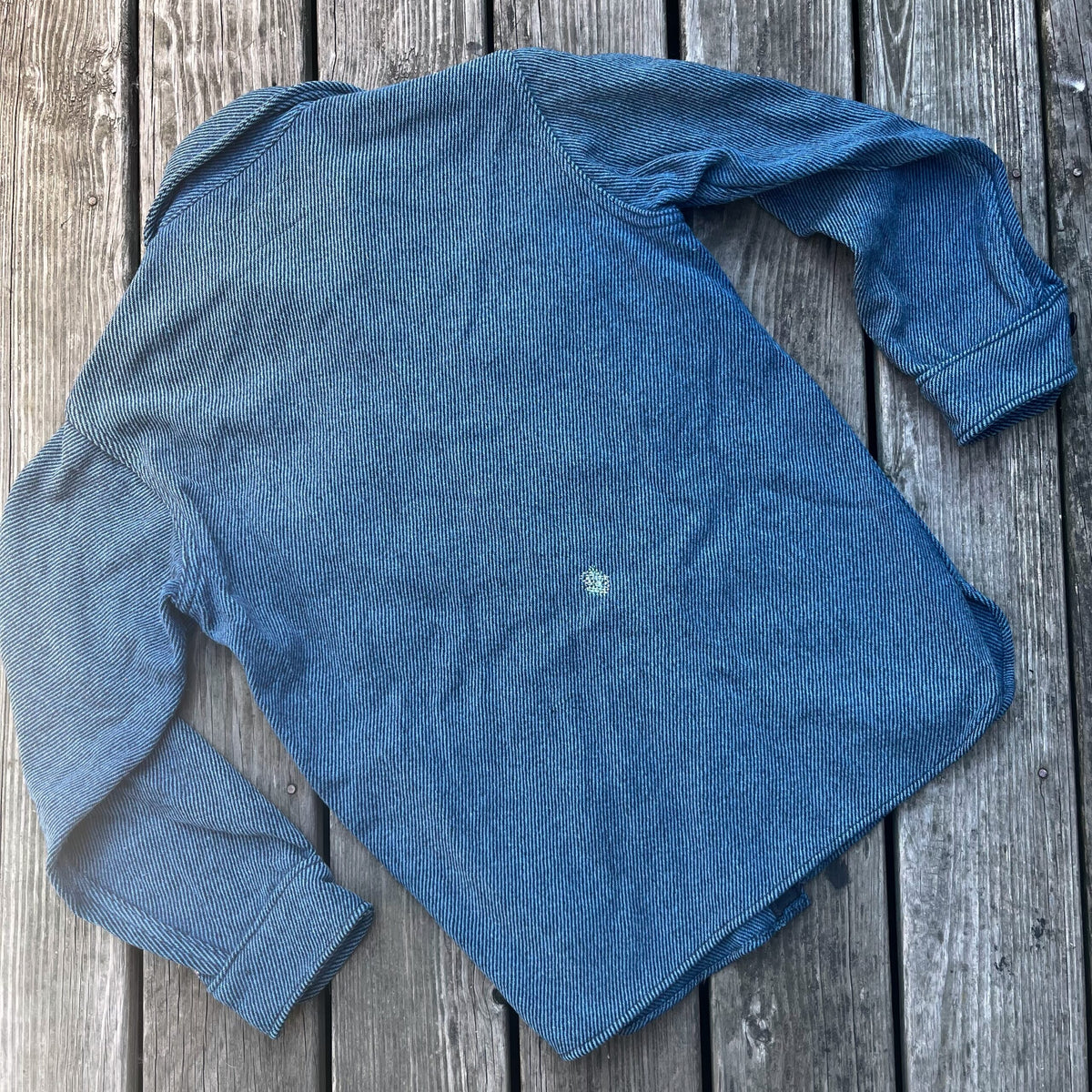 A blue wool shirt laying on a wooden deck.