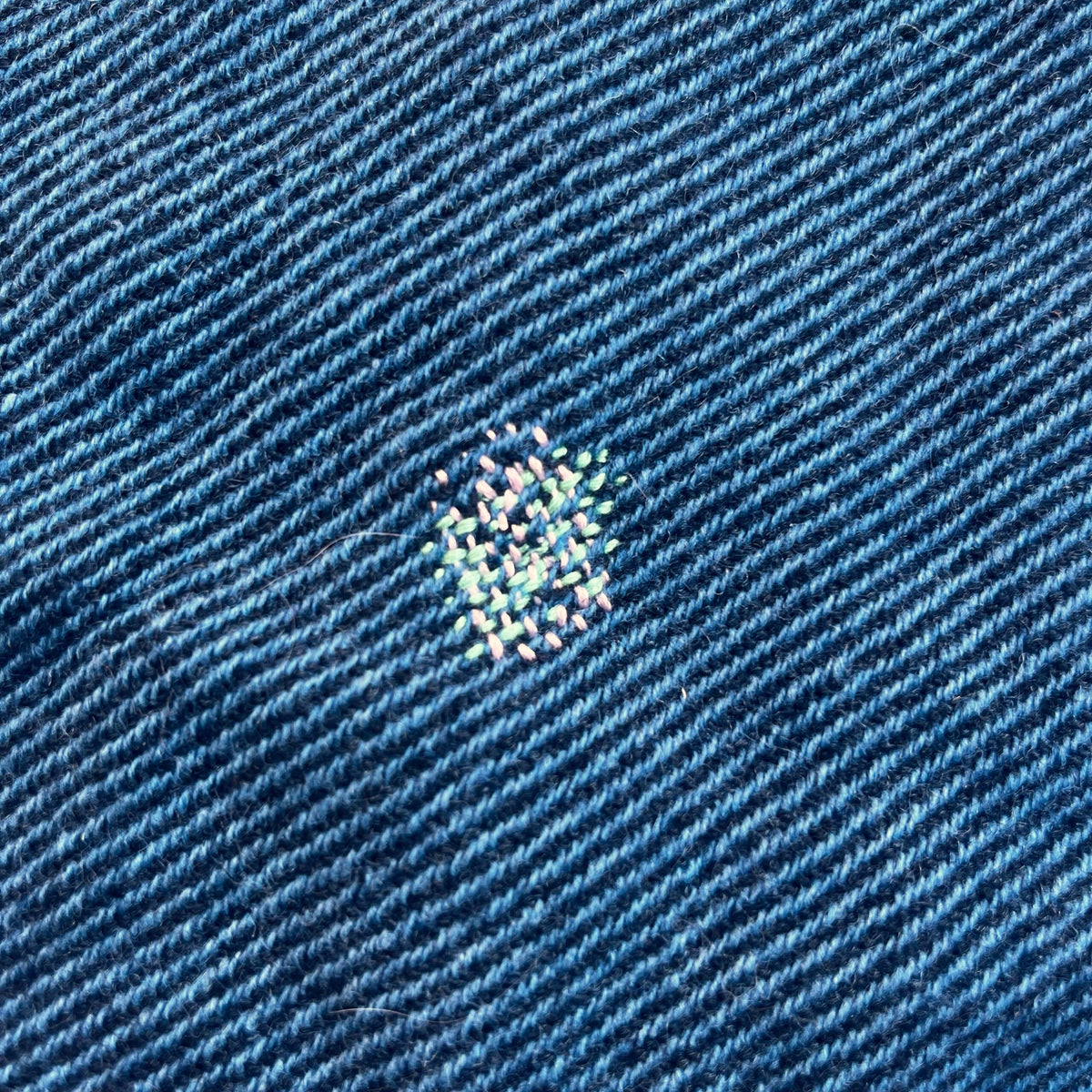 A close up of a blue wool shirt with a small square darn on it.