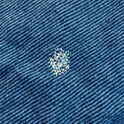 A close up of a blue wool shirt with a small square darn on it.