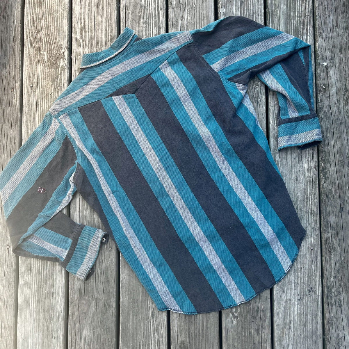 A blue and grey striped shirt on a wooden floor.