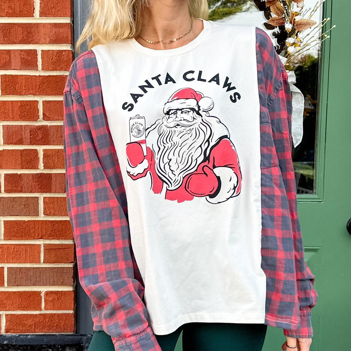 A woman wearing a santa claws t - shirt in front of a brick wall.
