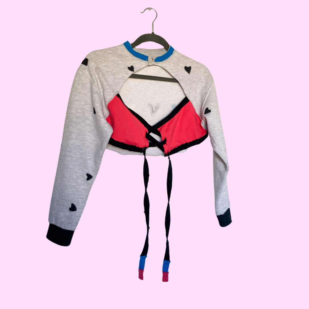A cropped sweater hanging on a pink background.