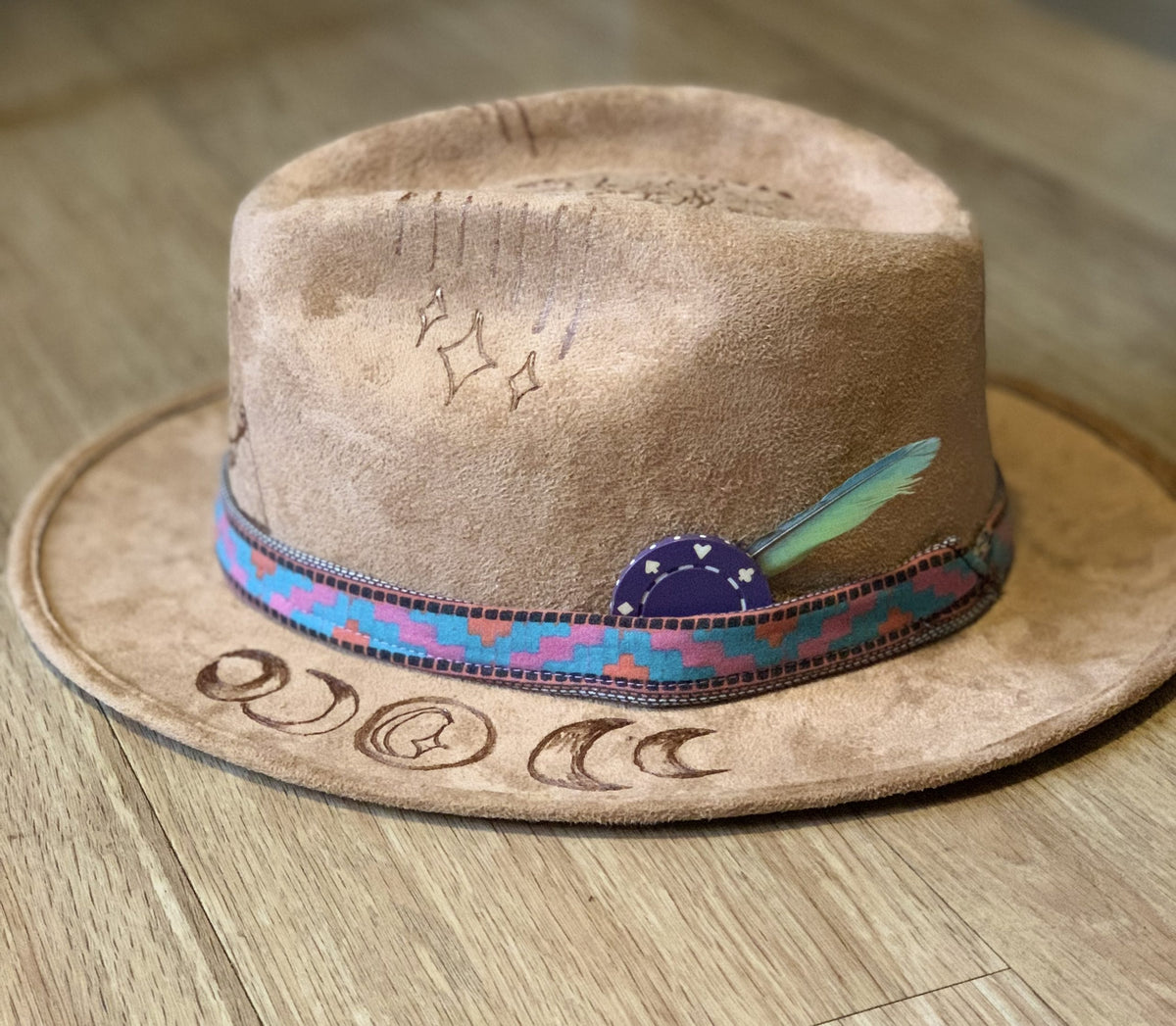 A suede hat wood burned with accessories with a feather on top of it.