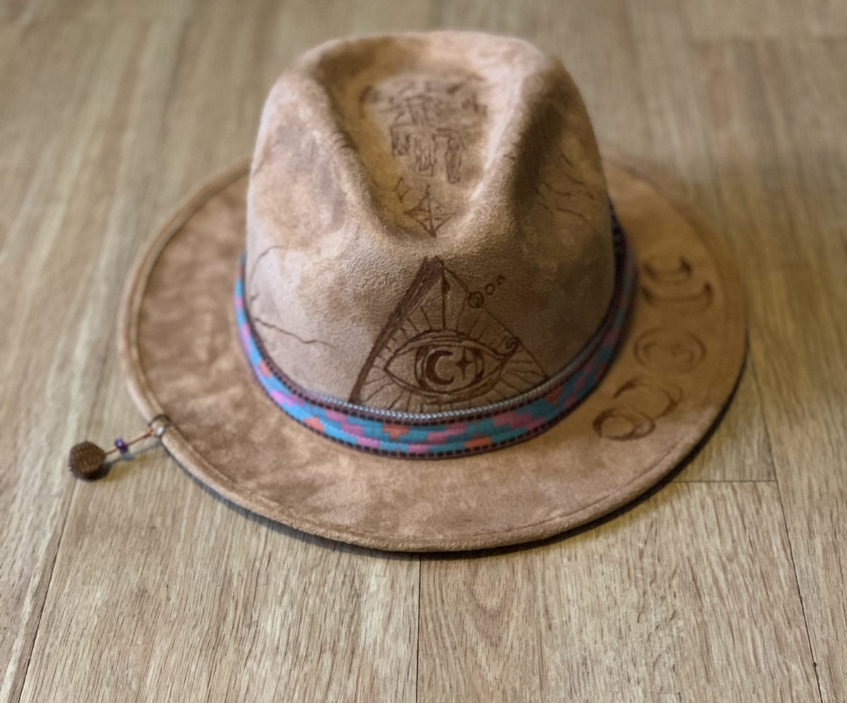 A suede hat wood burned with accessories sitting on top of a wooden floor.