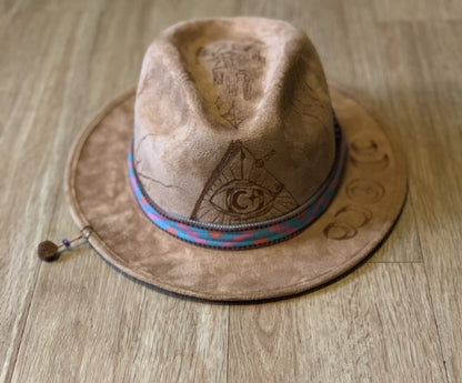 A suede hat wood burned with accessories sitting on top of a wooden floor.