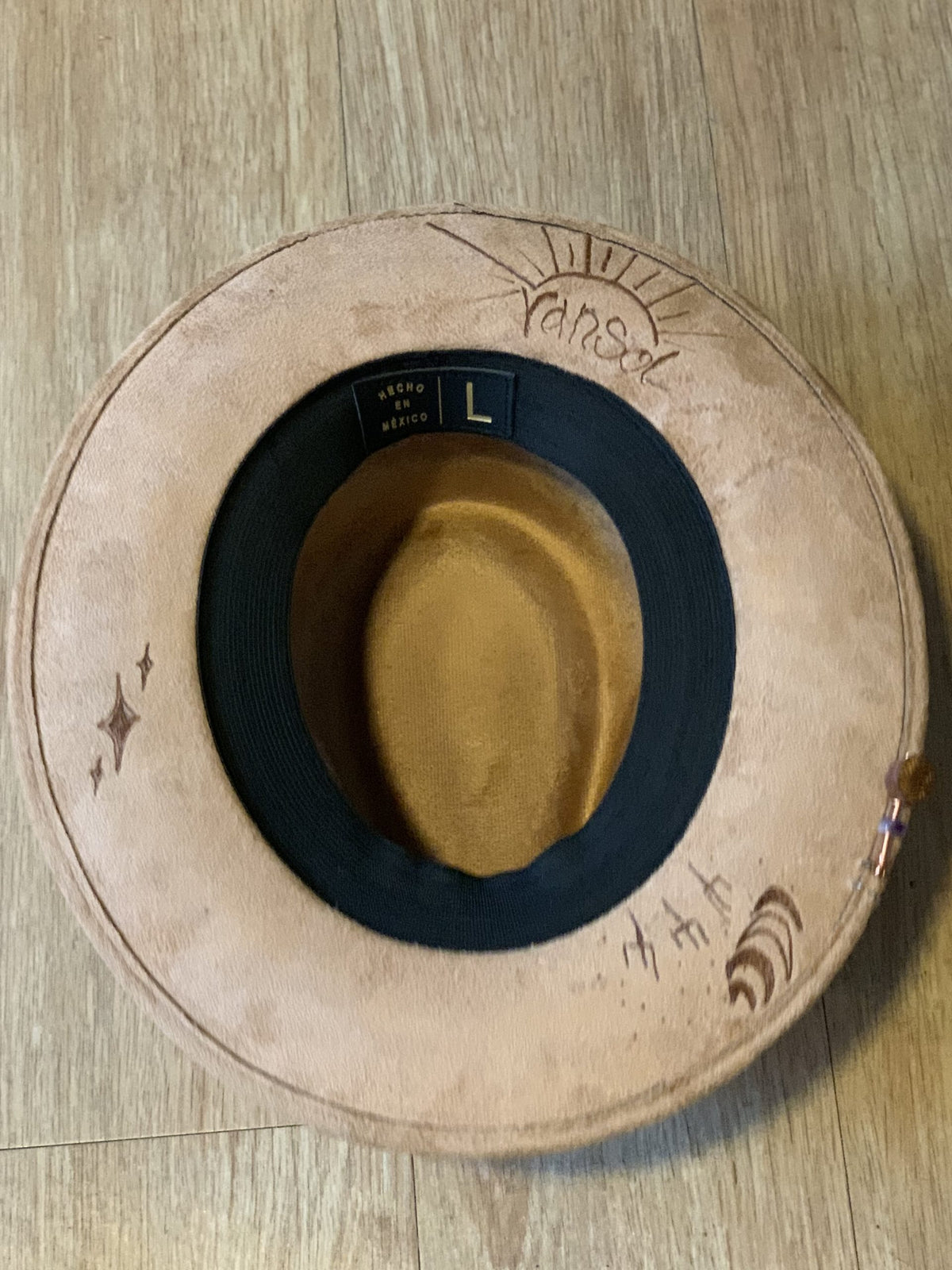 A suede hat wood burned with accessories sitting on a table.