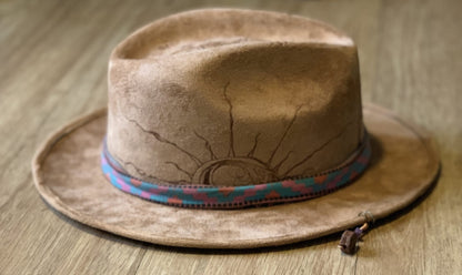 A suede hat wood burned with accessories sitting on top of a wooden table.
