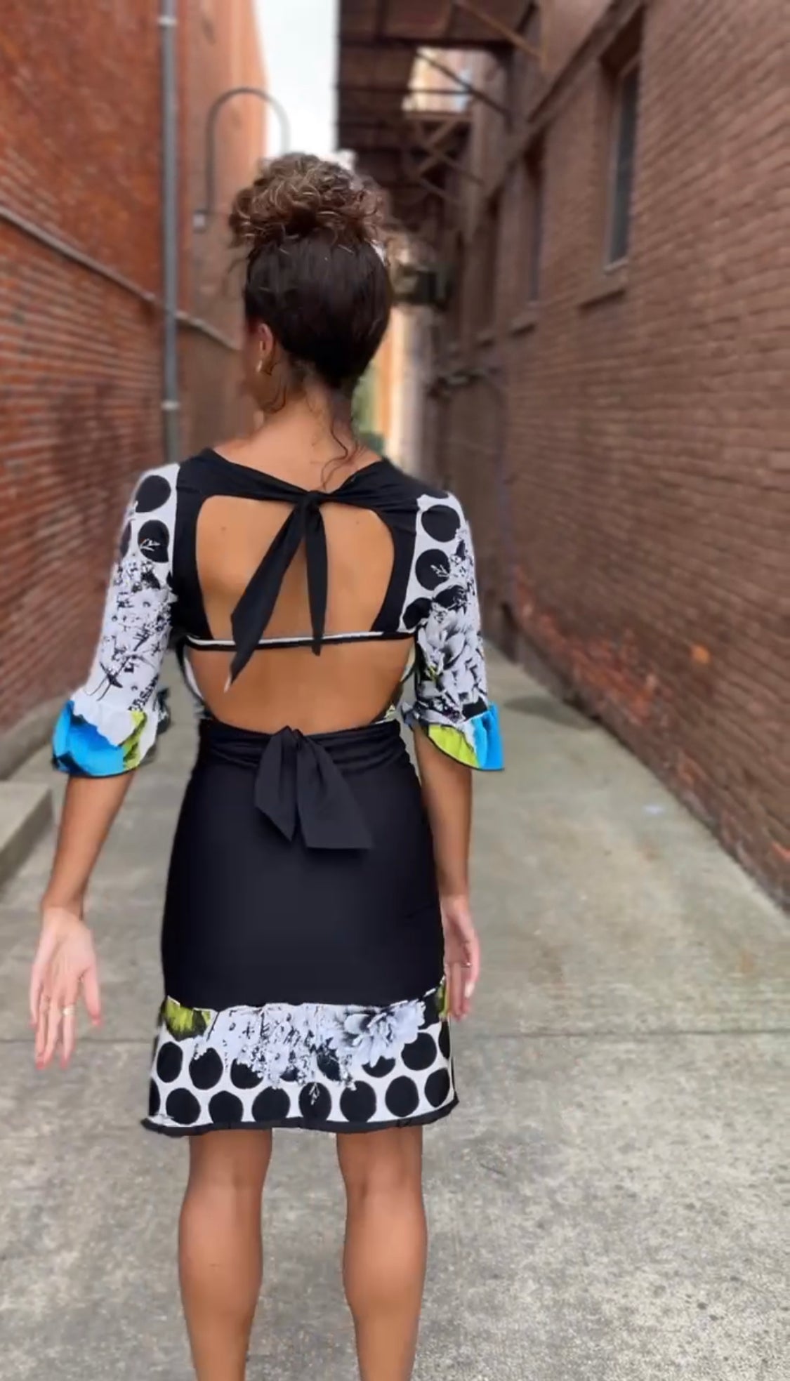 A woman walking down an alley in a black and white polka dot dress.