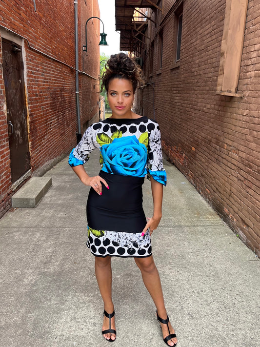 A woman in a blue and black dress posing in an alleyway.