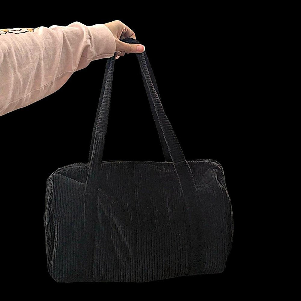 A person holding a black corduroy bag against a black background.