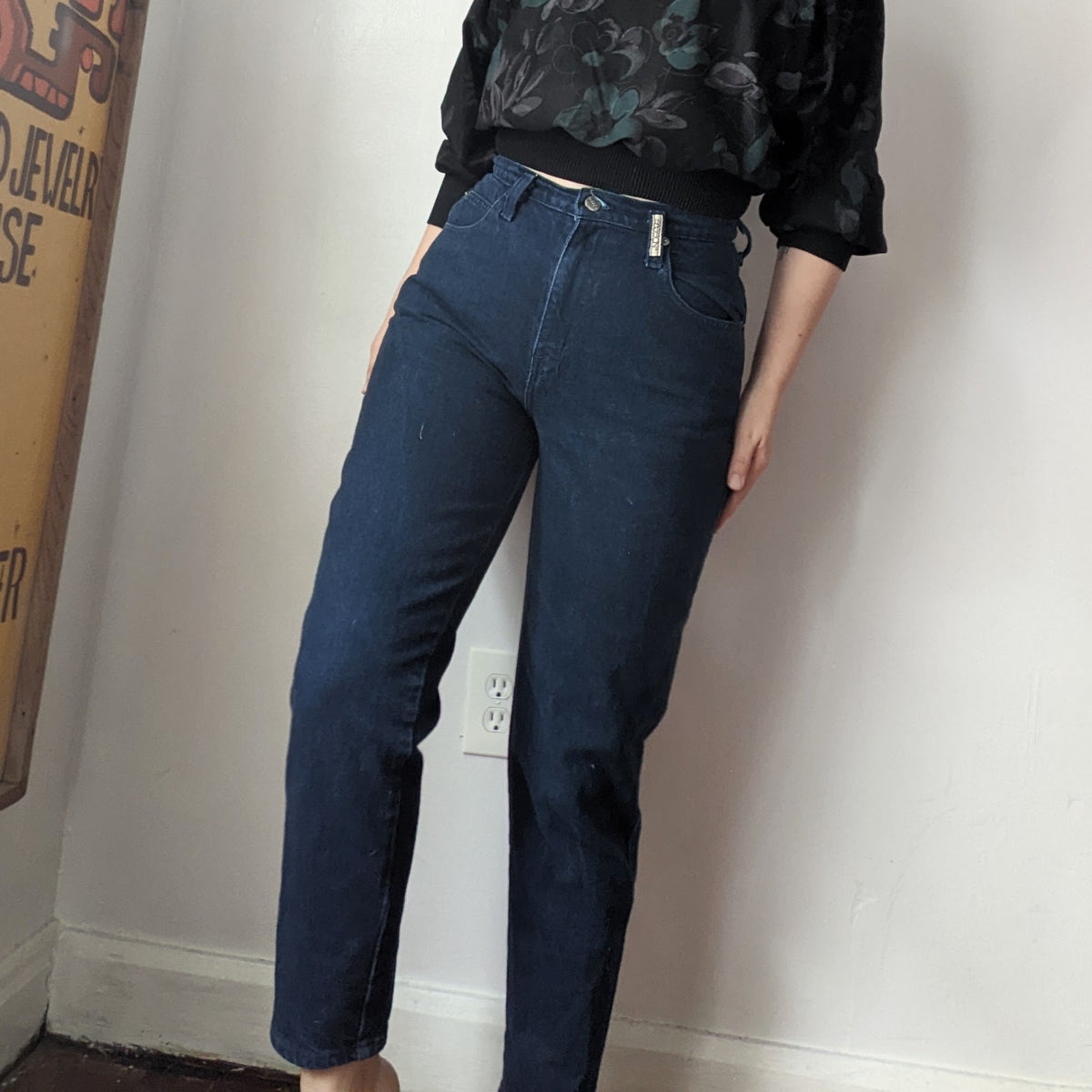 A woman standing next to a wall with her hands in the pockets of her Reworked Embroidered Rainbow Star Pocket Jeans.