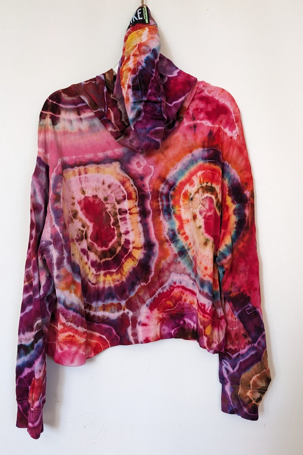 A tie dye hoodie hanging on a wall.