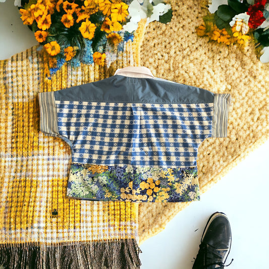 A traditional jacket with a geometric pattern and floral trim laid on a textured yellow rug, next to marigolds and a black shoe.