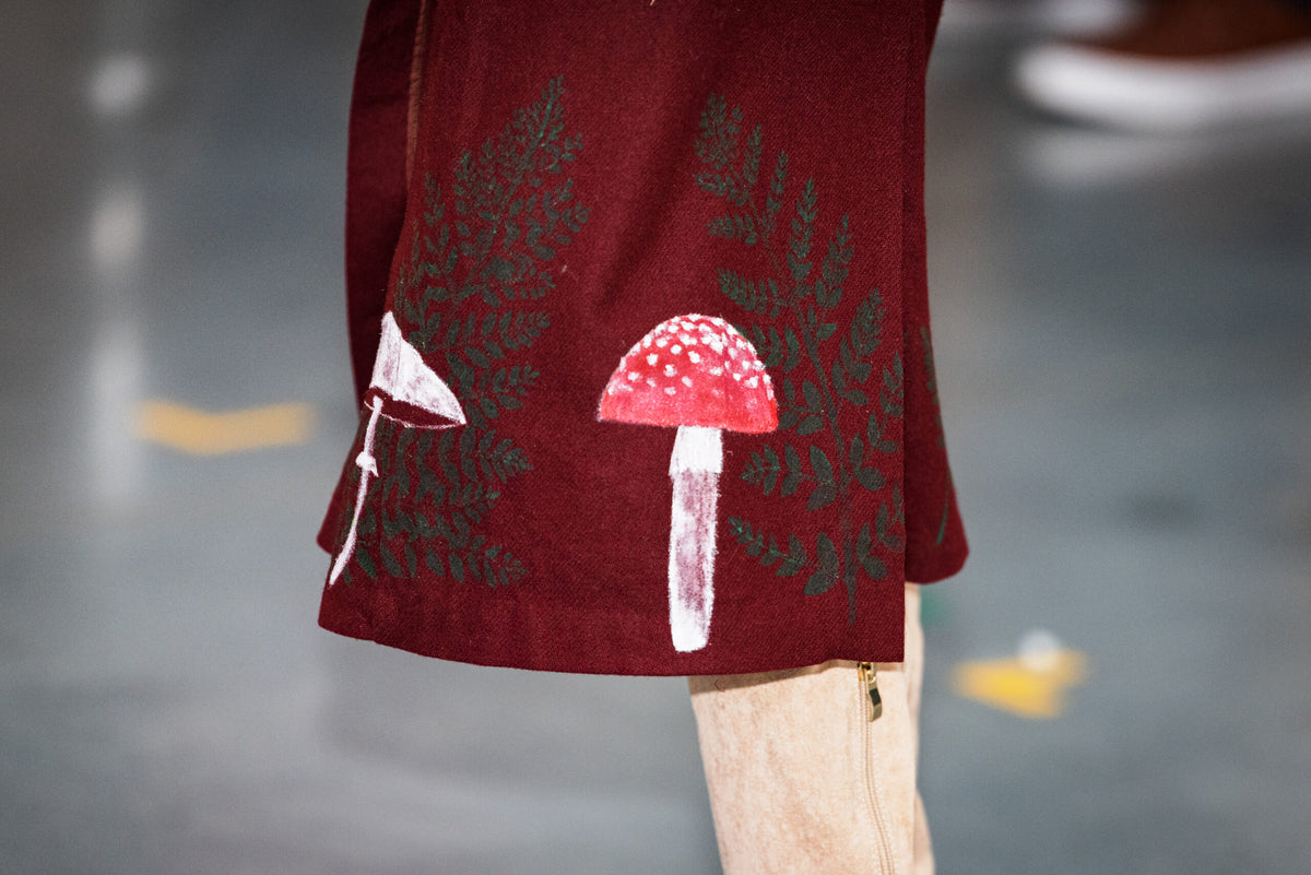 Bottom of maroon skirt with painted mushrooms and ferns on it