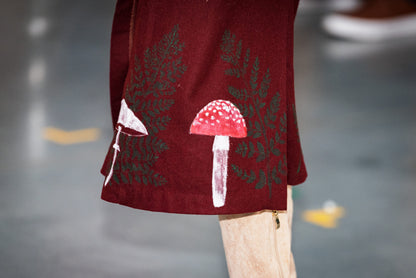 Bottom of maroon skirt with painted mushrooms and ferns on it