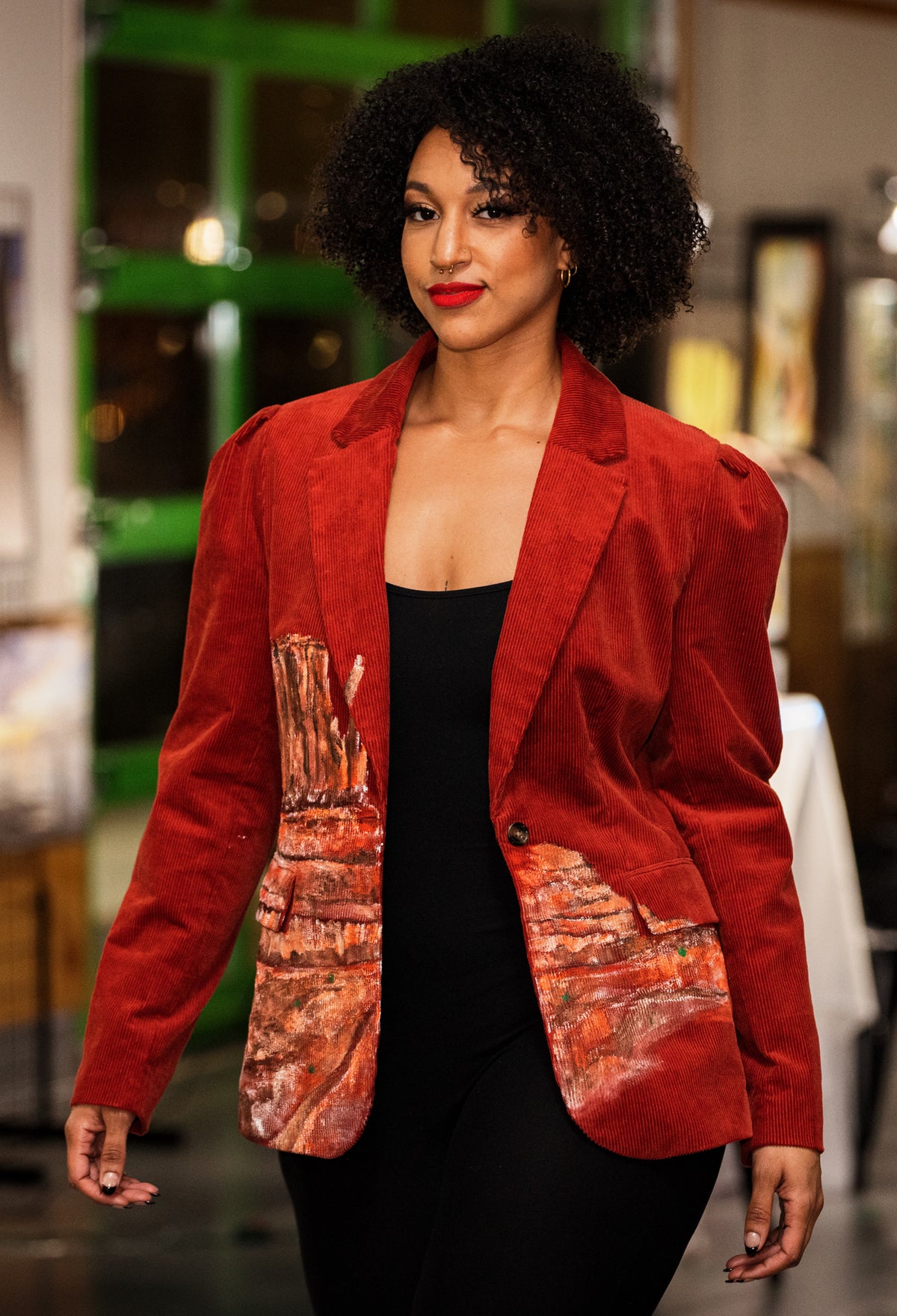 A woman wearing a red hand-painted blazer and black pants.