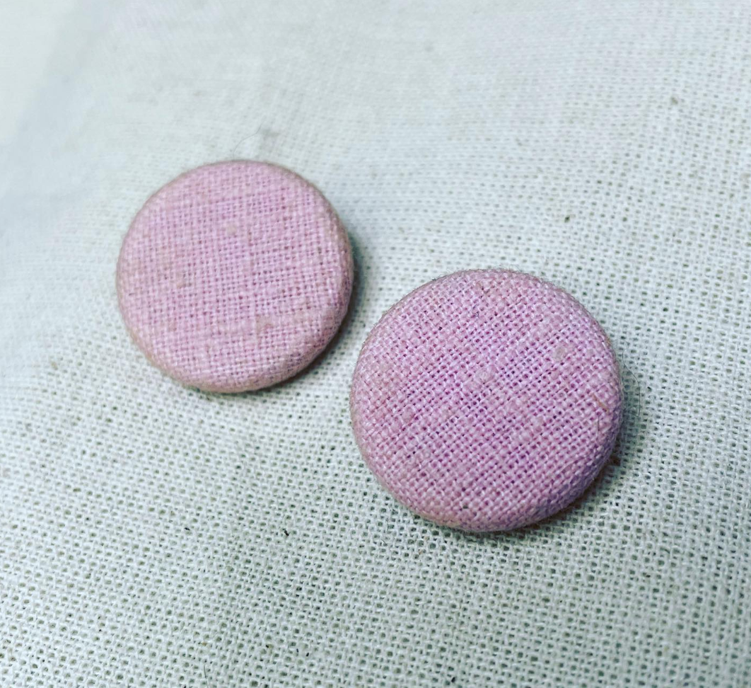 two pink buttons sitting on top of a white cloth.
