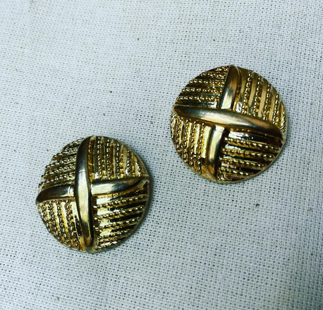 a pair of gold toned buttons sitting on top of a white cloth.