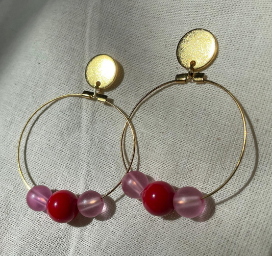 a pair of gold hoop earrings with pink and red beads.