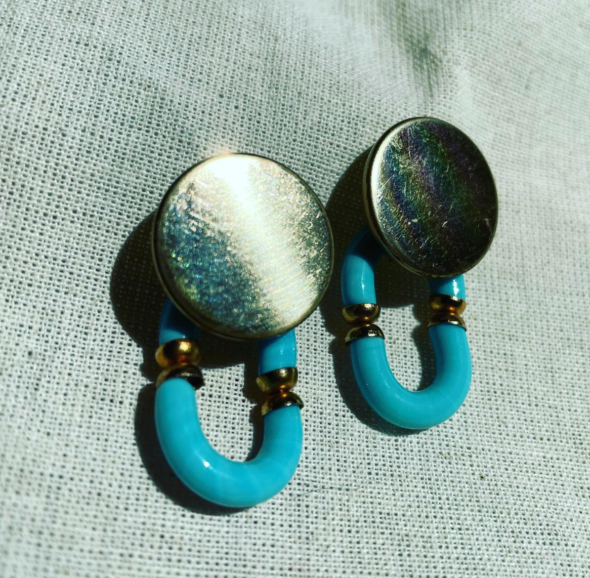 a pair of blue and gold earrings on a white cloth.