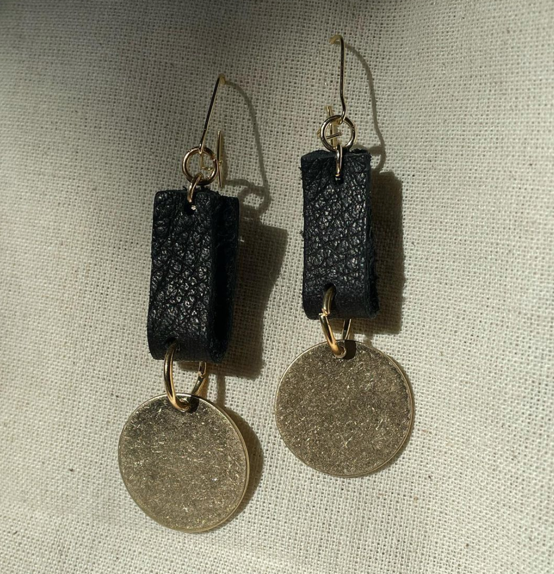 a pair of earrings with a coin hanging from it.