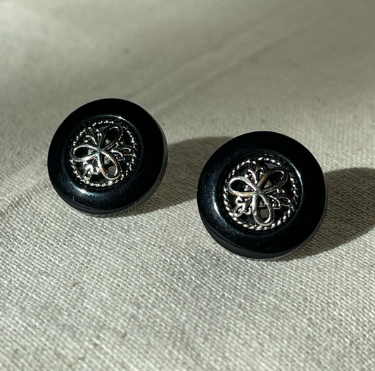 a pair of black and silver earrings sitting on top of a white cloth.