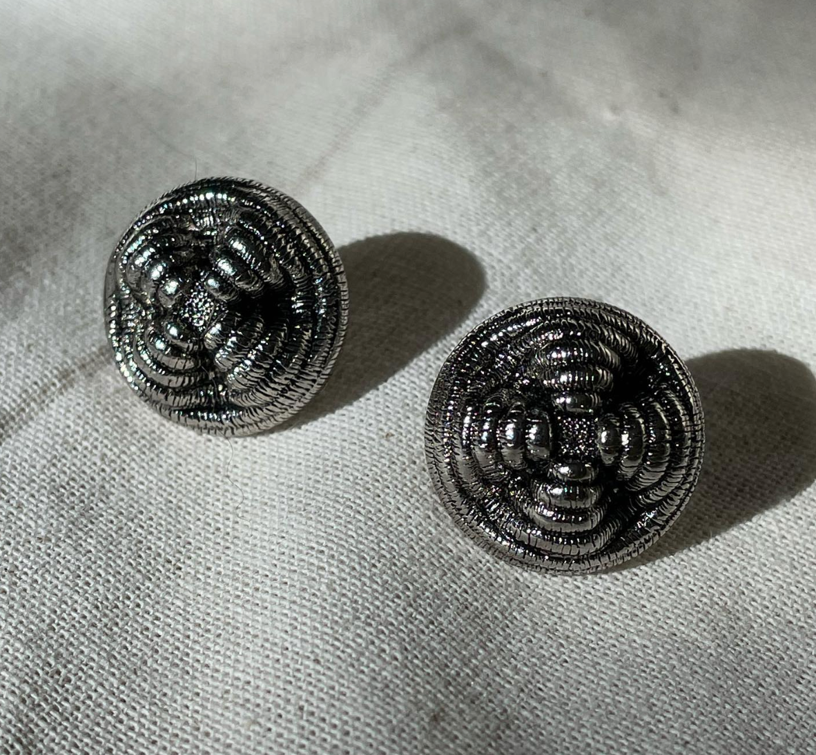a pair of earrings sitting on top of a white cloth.
