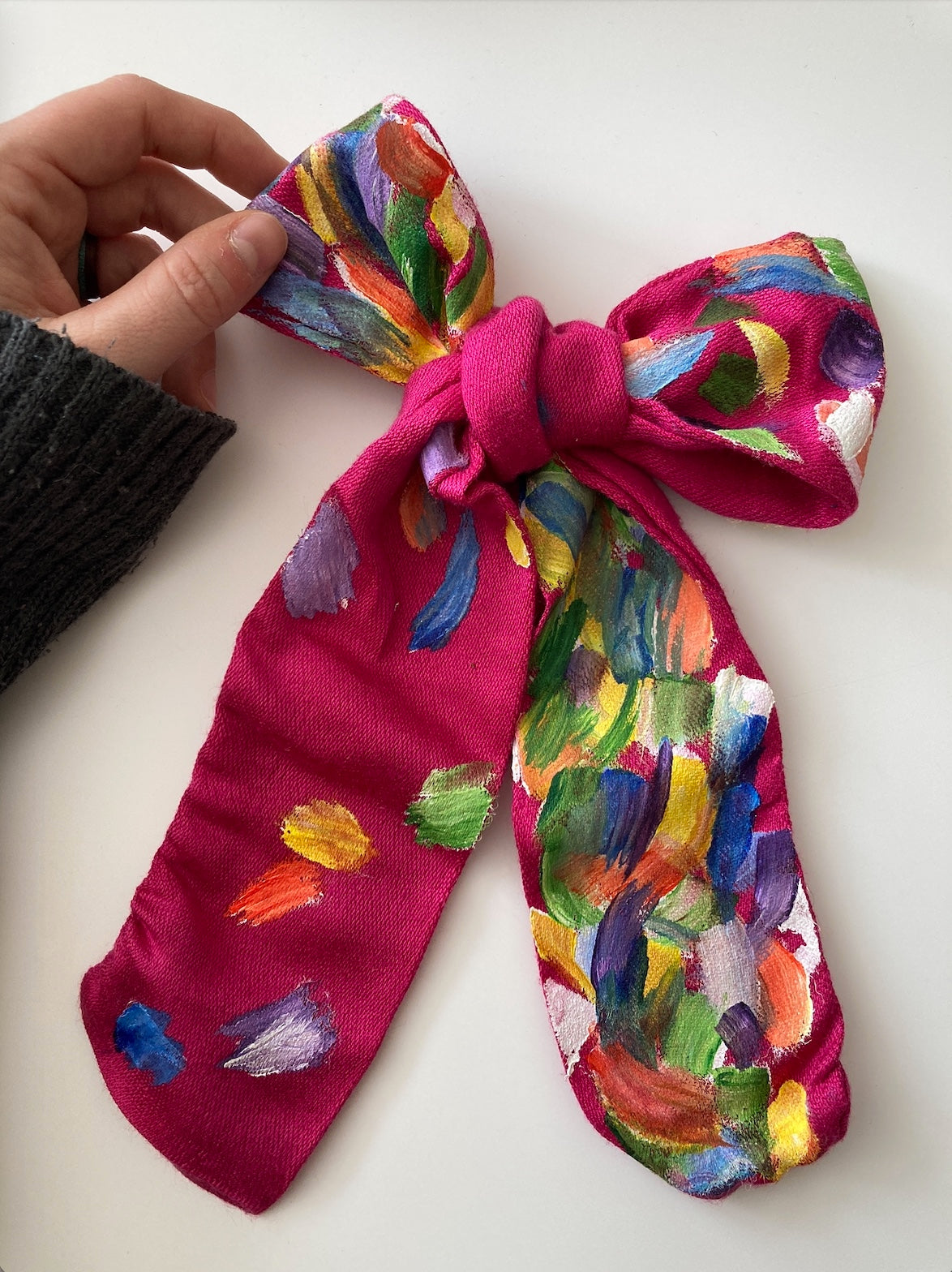 A person is holding a scarf with colorful paint on it.