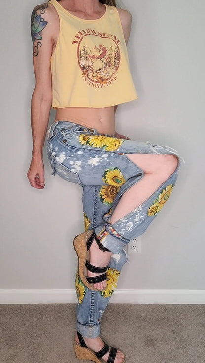 a woman in a yellow tank top and jeans posing in front of a wall.