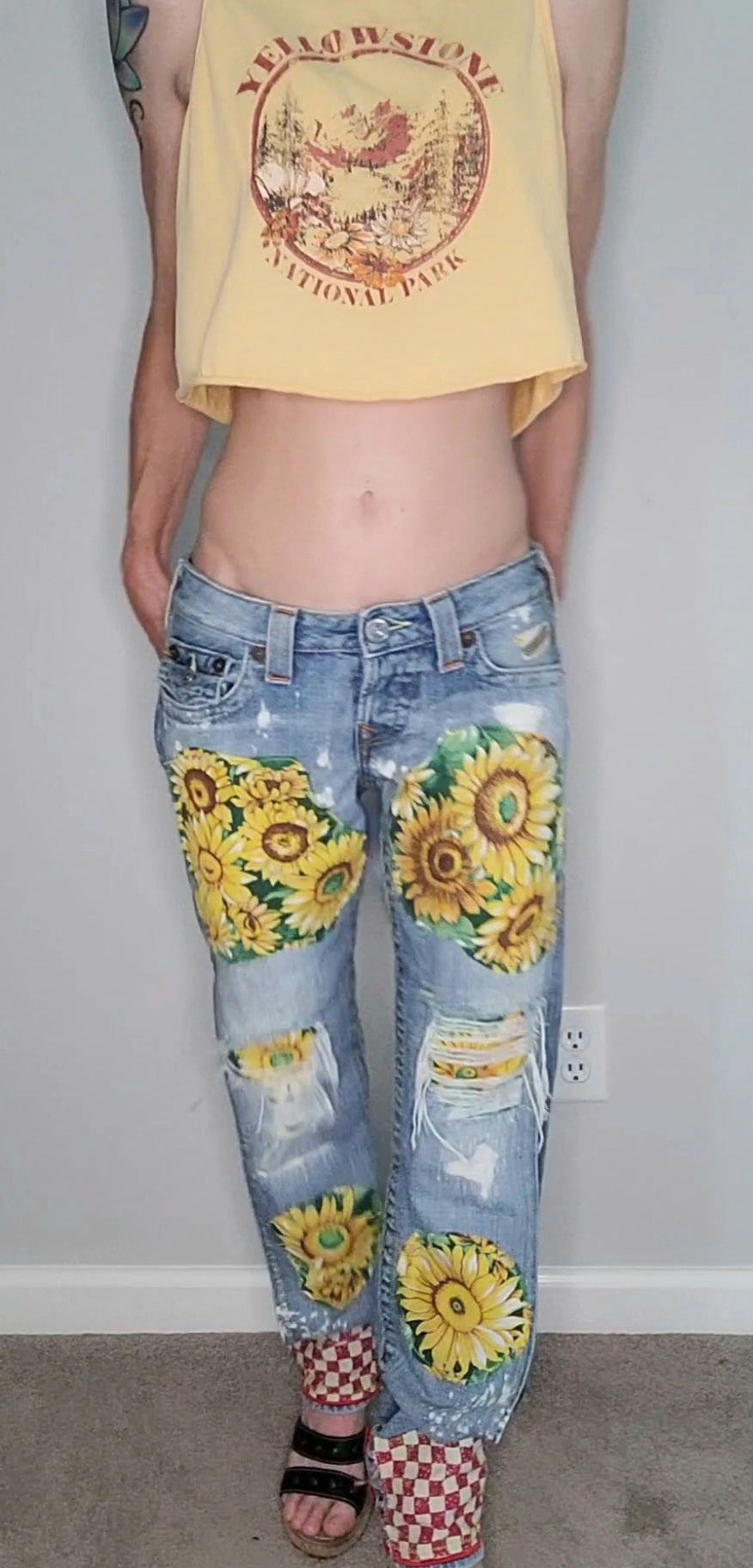 a woman wearing a yellow tank top and jeans with sunflowers on them.