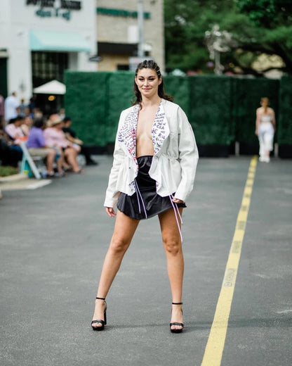 A woman in a LACE ICING Black Mini Skirt and jacket on a runway.