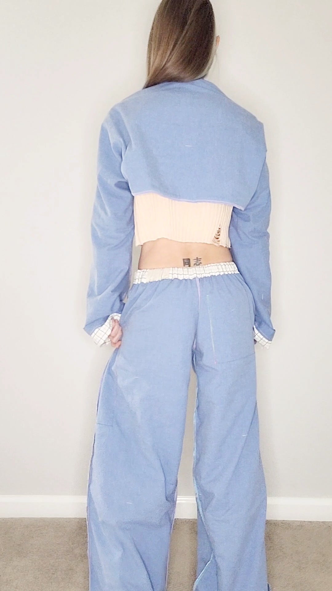 A woman is standing in a room wearing a blue jumpsuit.