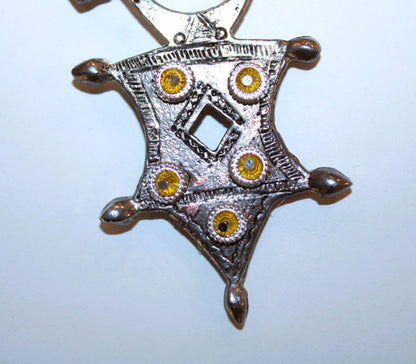 A silver Aztec style pendant with yellow stones on it.