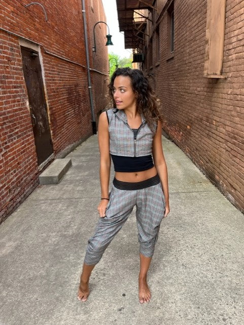 A woman standing in an alleyway wearing a plaid crop top and joggers.