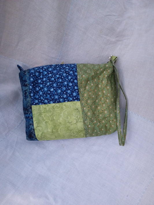A blue and green fabric wristlet purse with a patchwork pattern in Cottage Core style.