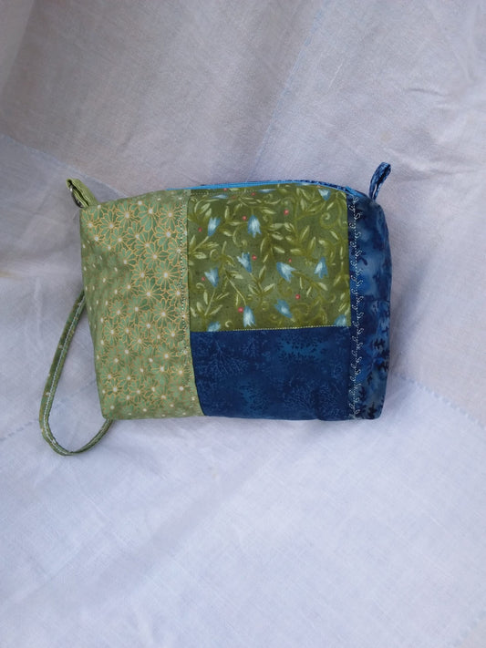 A blue and green fabric wristlet purse with a patchwork pattern in Cottage Core style.