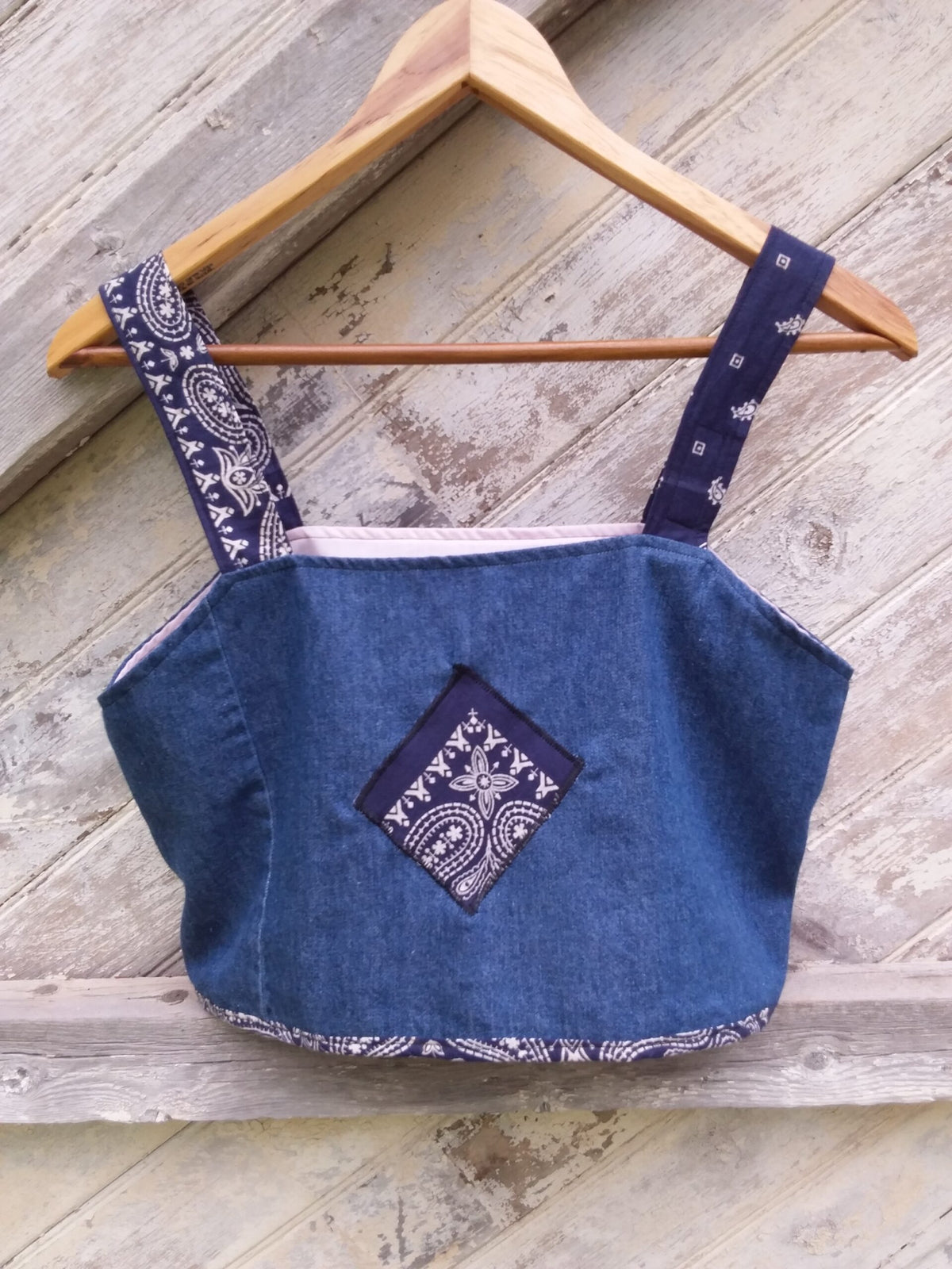 a blue denim crop top hanging on a wooden hanger.