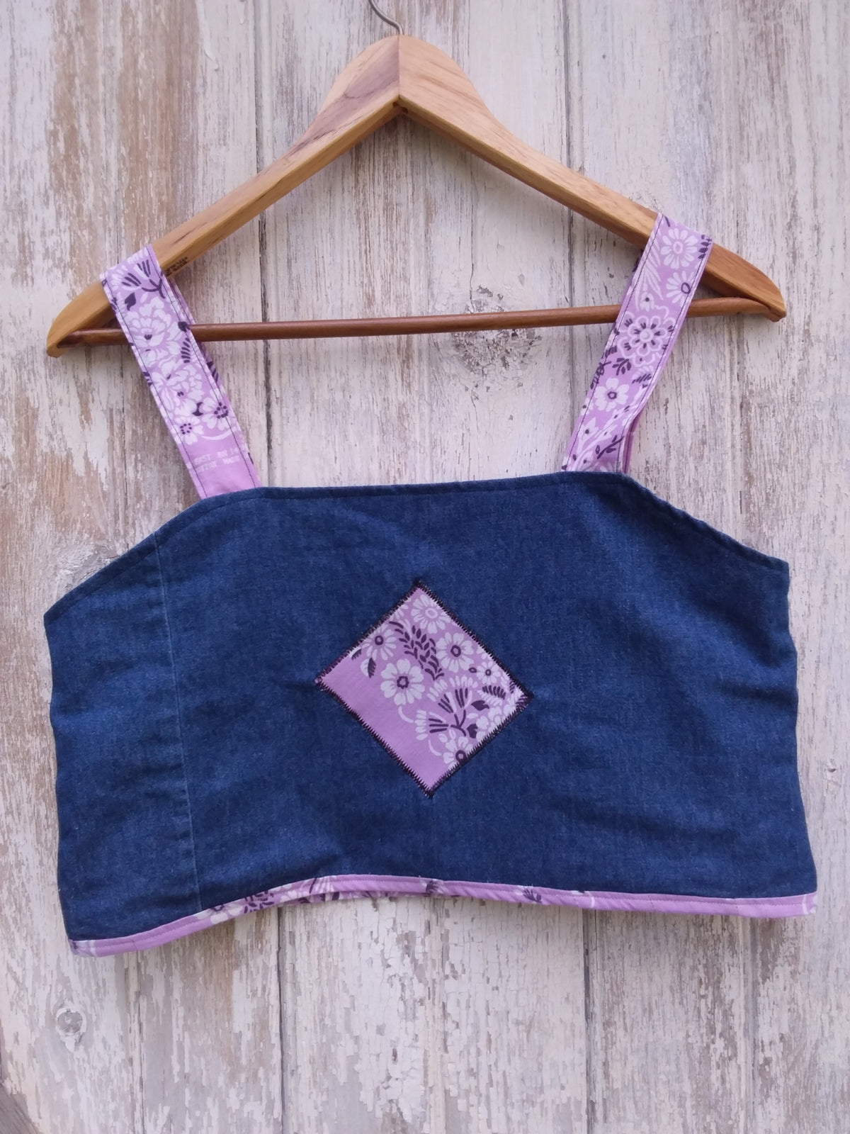 An upcycled denim and purple bandana fabric crop top on a wooden hanger