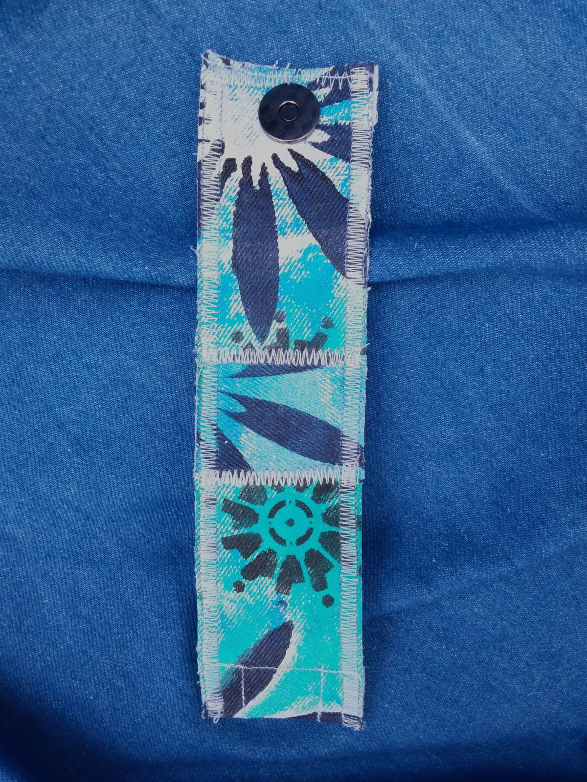 A hand painted, recycled denim cuff bracelet with a flower on it.