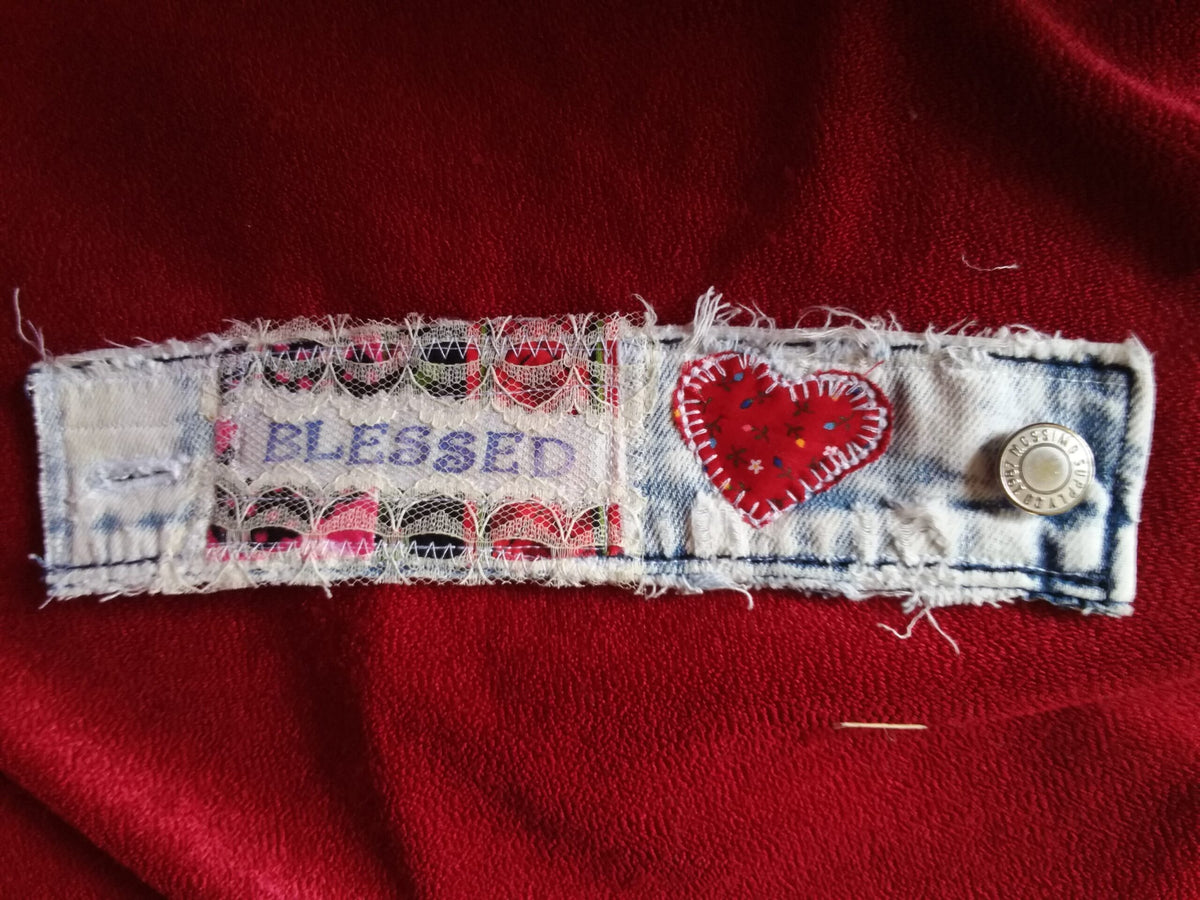A denim cuff bracelet with a heart and the word Blessed on it.