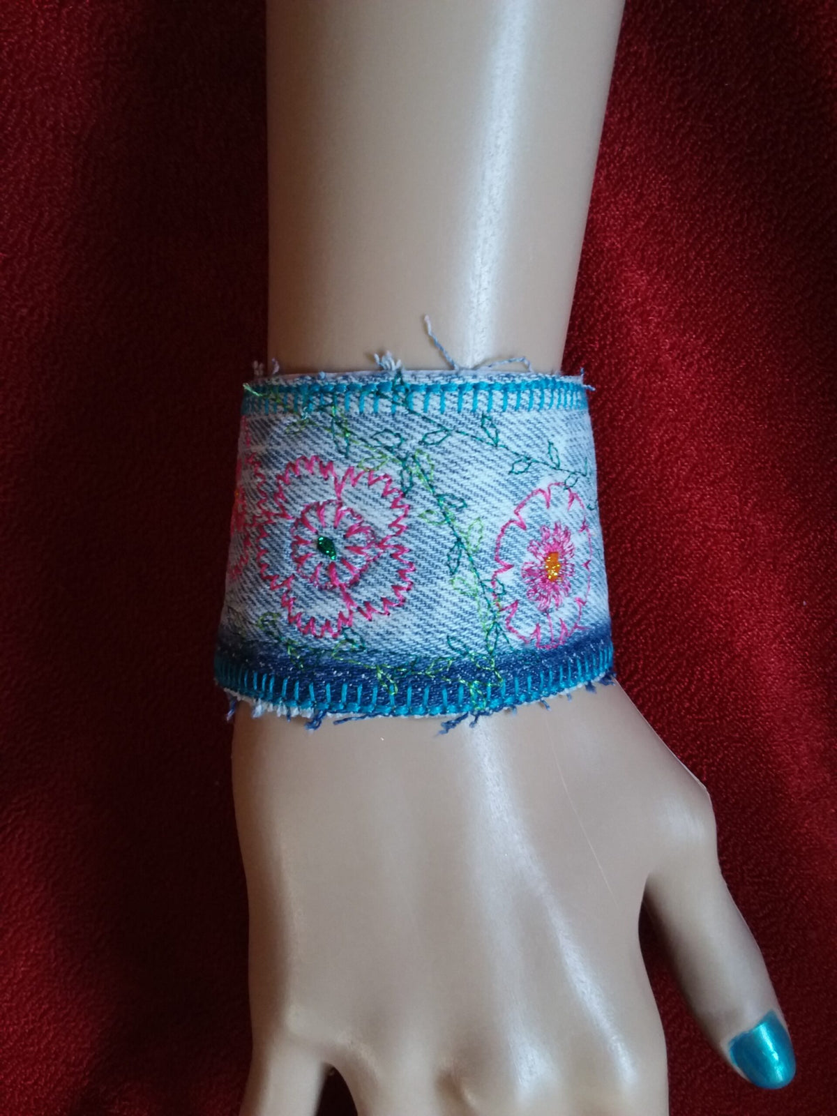 A denim cuff bracelet with embroidered flowers on it.