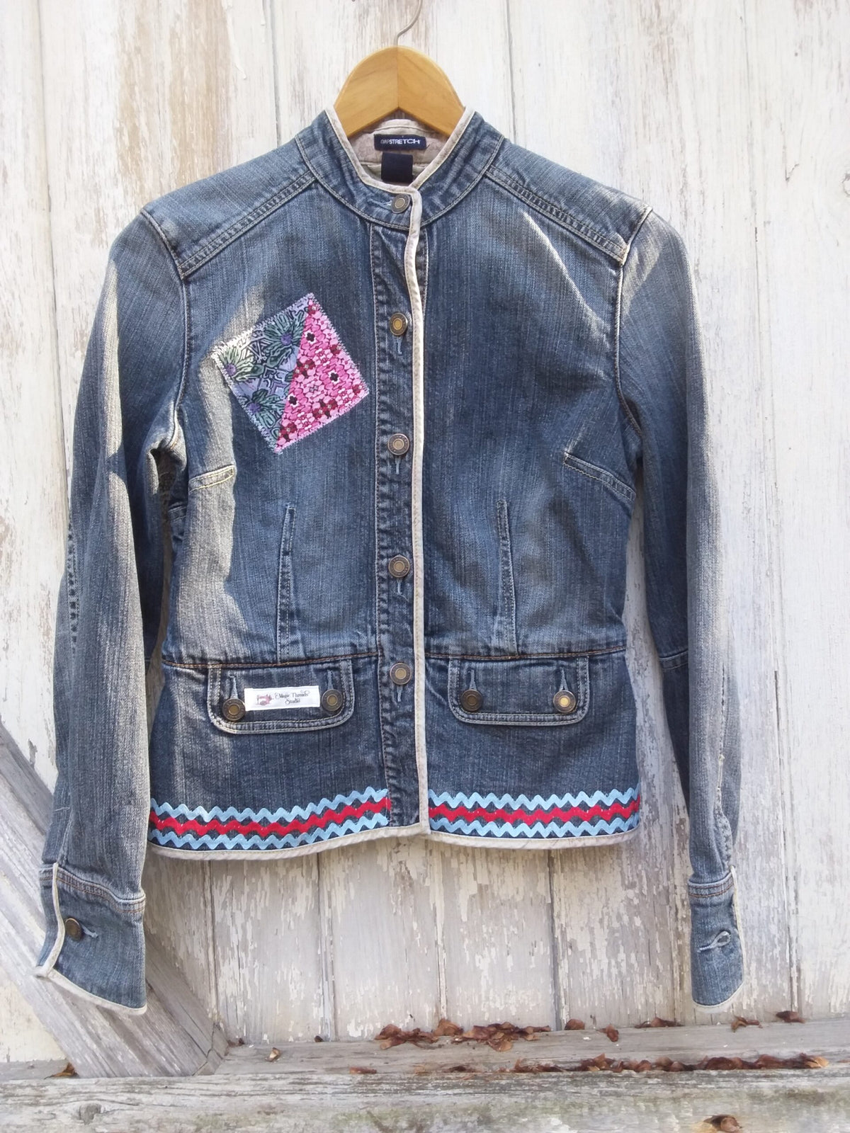 A denim jacket hanging on a wooden wall.