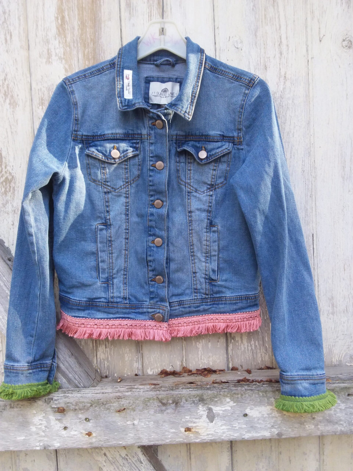 A denim jacket with fringes hanging on a wooden wall.