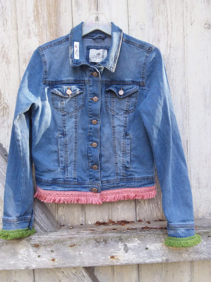 A denim jacket with fringes hanging on a wooden wall.