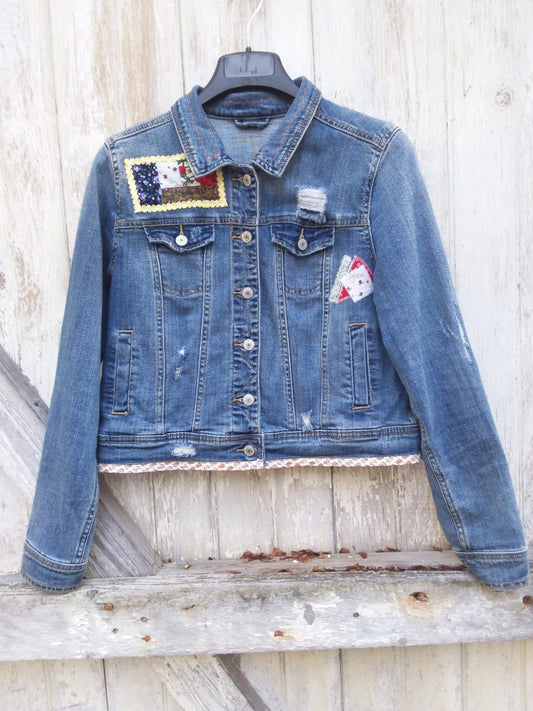 A denim jacket with patches hanging on a wooden wall.