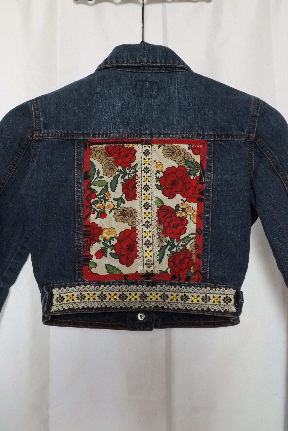 An upcycled cropped denim jacket with roses and lace on it