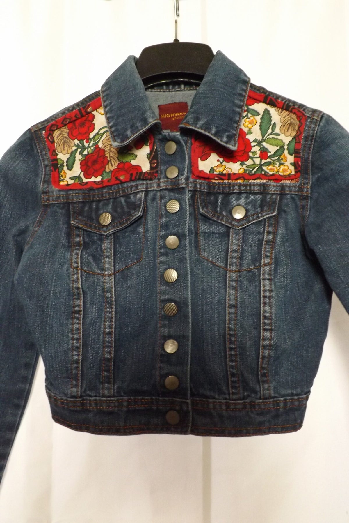 An upcycled denim jacket with roses and leaves on it.