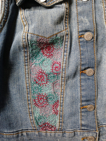 A denim vest with embroidered spirals on it.