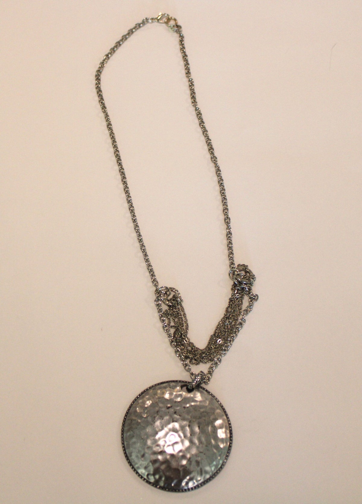 A silver necklace with a hammered disc on it.