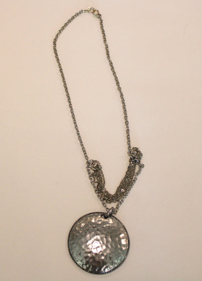 A silver necklace with a hammered disc on it.